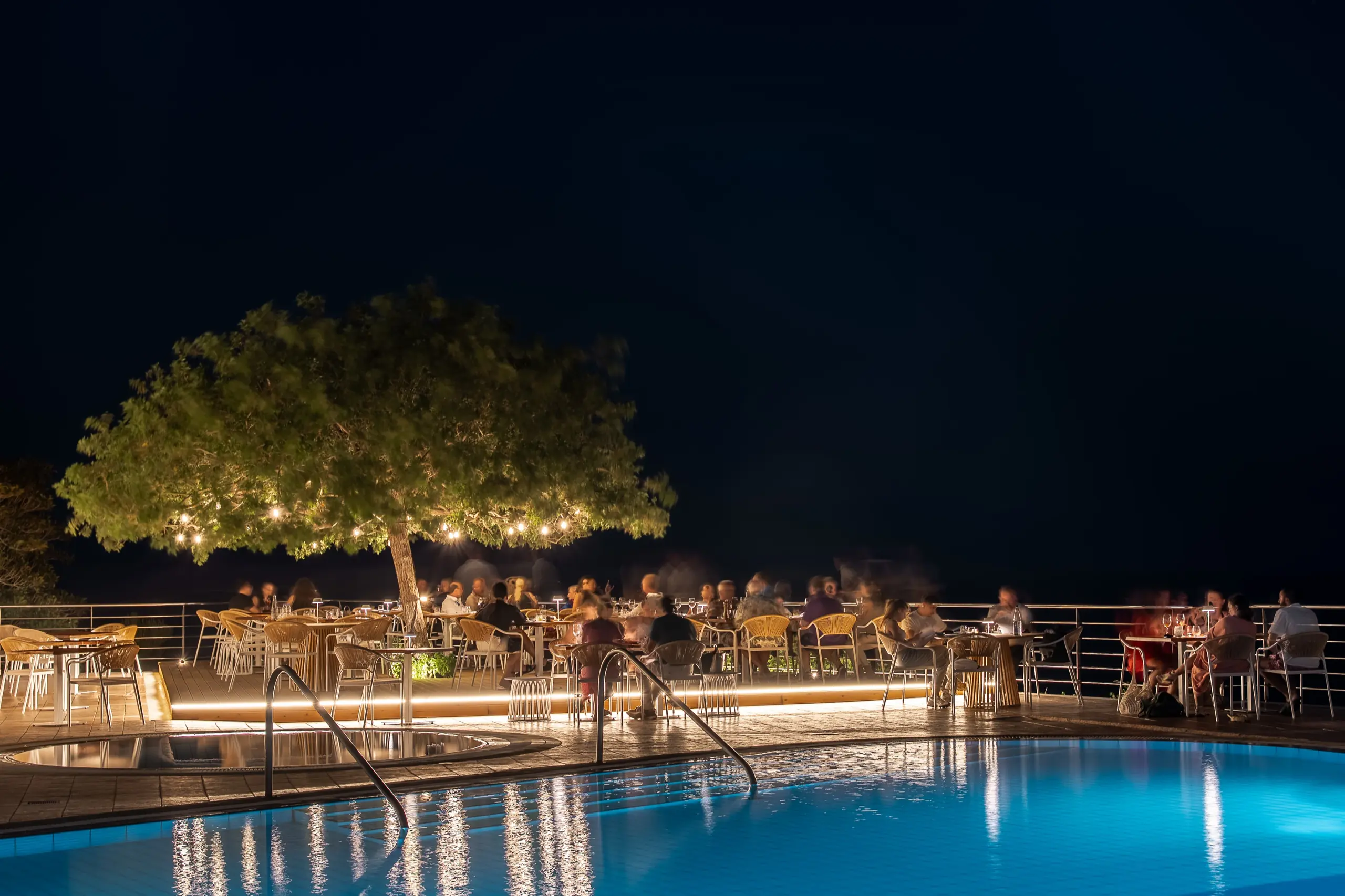 Evening view from the Thyrea terrace over the Cretan coastline, tables set under warm lighting